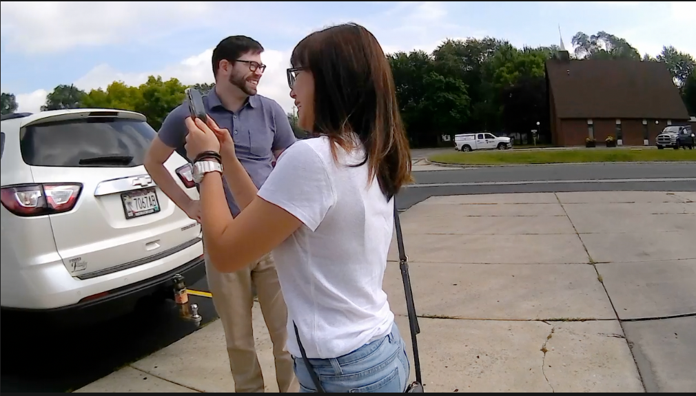 A photo of Venkat's two teammates in front of a car. One is taking photos with her phone, and the other teammate is looking away from the camera and smiling.